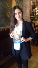 Η Χριστίνα Σαρρή στην παρουσίαση του βιβλίου της. Κρατάει μπροστά της ένα αντίτυπο και χαμογελάει.