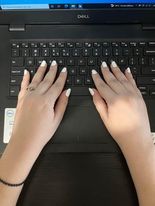 Τα χέρια της Χριστίνας ακουμπισμένα επάνω στο πληκτρολόγιο ενός μαύρου λάπτοπ. Τα νύχια της είναι βαμμένα λευκά, ενώ δύο νύχια σε κάθε χέρι έχουν επίσης και ασημένιο Γκλίτερ.