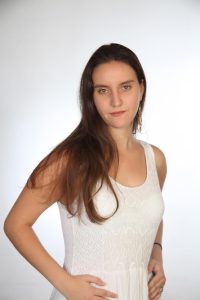 Η Χριστίνα Σαρρή, όρθια, με τα χέρια στη μέση. Εχει τα μαλλιά της αφημένα κάτω και είναι μακιγιαρισμένη. Φοράει λευκό φόρεμα και λευκά, κρεμαστά σκουλαρίκια σε σχήμα φτερών.