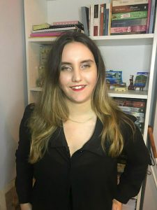 Η Χριστίνα Σαρρή με μαύρο πουκάμισο μπροστά από τη βιβλιοθήκη της