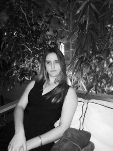 Ασπρόμαυρη φωτογραφία με τη Χριστίνα Σαρρή καθισμένη στο καναπεδάκι μιας καφετέριας