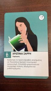 Φωτογραφία που δείχνει μια κάρτα επιτραπέζιου παιχνιδιού επάνω σε ένα ξύλινο τραπέζι. Στην κάρτα απεικονίζεται η Χριστίνα Σαρρή σε κόμικ, να κρατάει ένα ανοιχτό βιβλίο μπροστά της σαν να το διαβάζει. Επάνω γράφει: «Χριστίνα Σαρρή, τύφλωση» και κάτω: «Κατέκτησε το πρώτο βραβείο διηγήματος σε πανελλήνιο, σχολικό, λογοτεχνικό διαγωνισμό. Σπουδάζει ψυχολογία και συγγράφει ποίηση, διηγήματα και μυθιστορήματα». Οι λεπτομέρειες του κόμικ είναι πανομοιότυπα σχεδιασμένες, όπως στην πραγματική φωτογραφία της Χριστίνας που ακολουθεί.