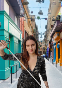 Η Χριστίνα Σαρρή, κρατώντας ένα λευκό μπαστούνι διαγώνια μπροστά της.
Βρίσκεται έξω στο δρόμο, φοράει μπλε φόρεμα και χαμογελά ελαφρώς.
