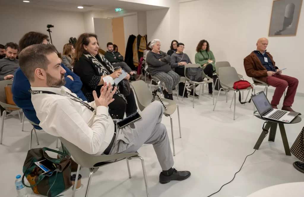 Αίθουσα συνεδριάσεων. Κόσμος καθισμένος σε καρέκλες.
