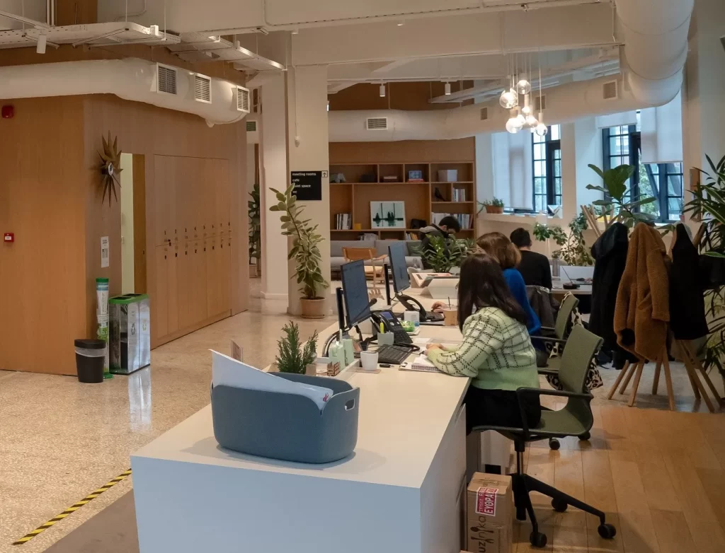 Κεντρικός χώρος του SPACES. Δεξιά το μεγάλο γραφείο της γραμματείας και στο βάθος καθιστικό με καναπέ και πολυθρόνες, μπροστά από βιβλιοθήκη.
