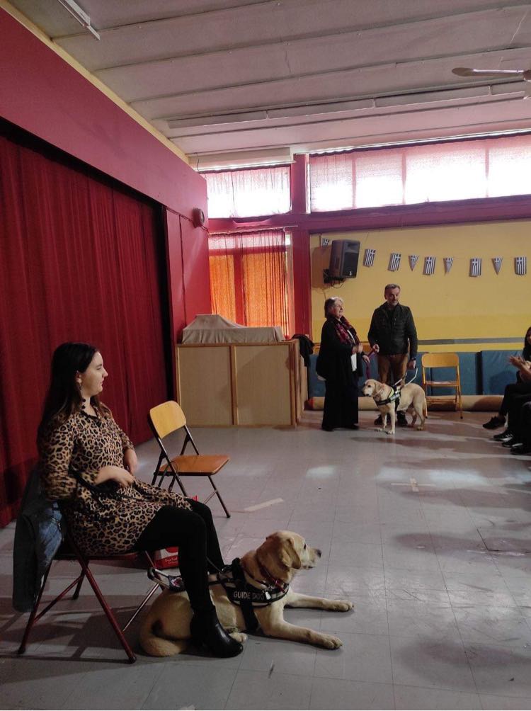 Η Χριστίνα Σαρρή καθισμένη με τη Λούνα ξαπλωμένη κάτω από τα πόδια της, φορώντας το ειδικό σαμάρι.
Πίσω στέκονται η κυρία Ζωή Γερουλάνου με το διευθυντή του σχολείου και την Ίρμα.