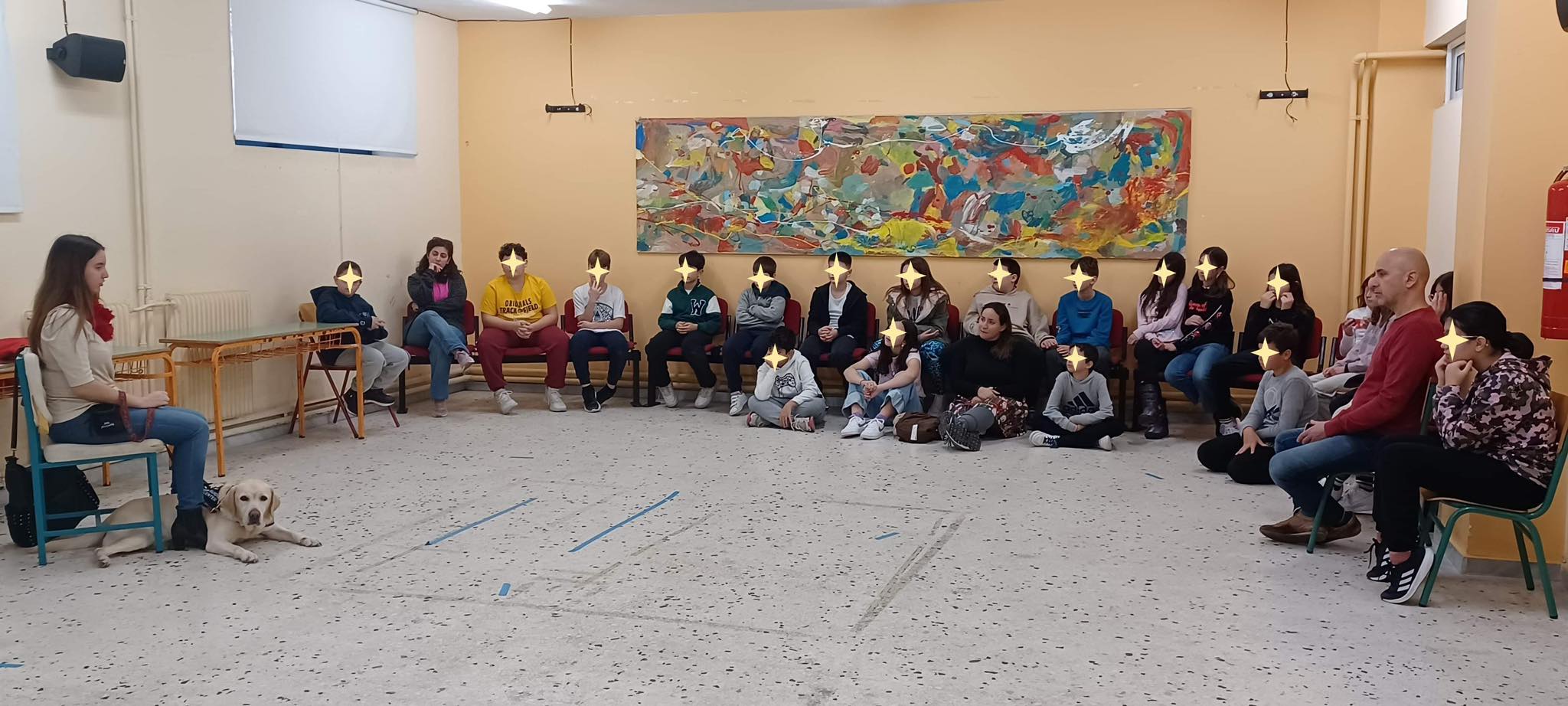 Η Χριστίνα σε μια μεγάλη αίθουσα δίνει ομιλία με τη Λούνα πλάι της και τα παιδιά κι οι εκπαιδευτικοί την παρακολουθούν.