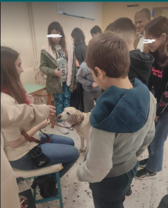 Η Χριστίνα χαμογελαστή κρατάει από το λουράκι τη Λούνα που έχει βγάλει το γιλέκο κι απολαμβάνει τα χάδια των παιδιών γύρω της.